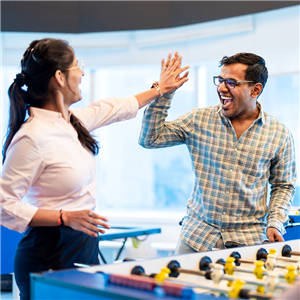 Two Capital One India associates stand next to a foosball table and high five